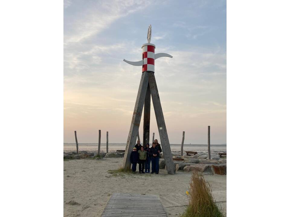 Gruppenfoto am SStrand unter hohen Holzstämmen.
