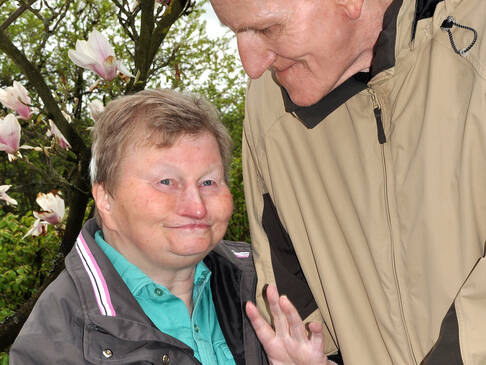 Ein älterer Herr steht und schaut eine sitzende Frau an.