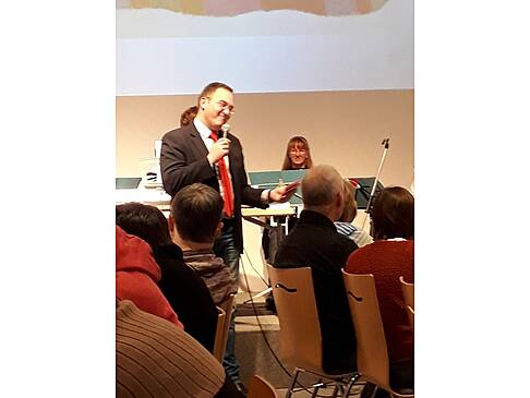Ein Mann spricht mit Mikrofon vor Puplikum.