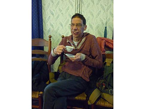 Ein Mann hat seine Teetasse und Untertasse in der Hand und lächelt.
