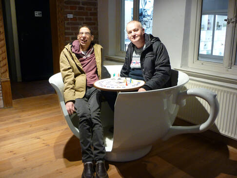 Zwei Männer sitzen in einer übergroßen Kaffeetasse an einem Tisch.