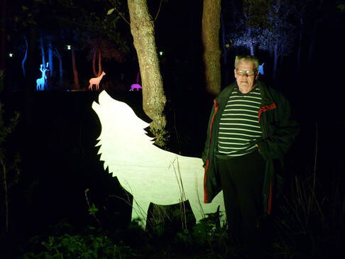 Ein Mann steht neben einer Wolfsfigur in weiß.