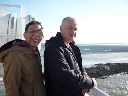 Zwei Männer lächeln, im Hintergrund das Meer.