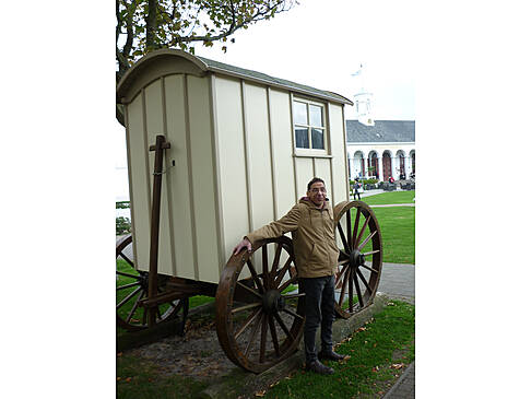 Ein Mann steht vor einem alten Pferdewagen.