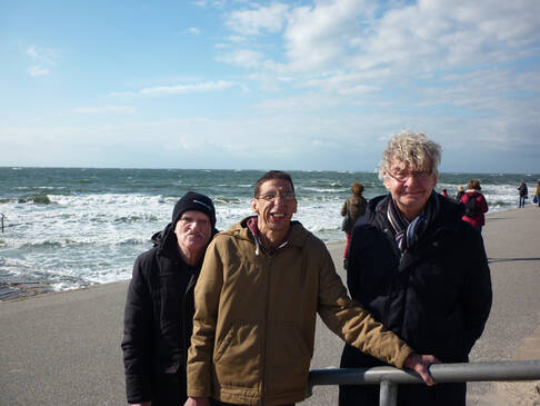 Drei Männer stehen am Strand und lächeln.