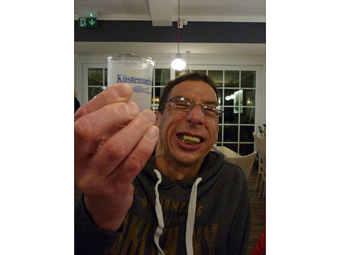 Ein Mann zeigt einen Schnaps und lächelt.