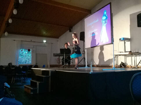 Ein Mann am Keyboard und eine Frau im Kleid auf der Bühne.