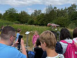 Eine Gruppe von Menschen, darunter mehrere Kinder, steht auf einem Weg in einem Park. Ein Jugendlicher macht mit seinem Smartphone ein Foto von einem Informationsschild.