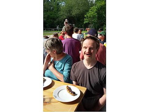 Mehrere Personen sitzen an Tischen in der Sonne.