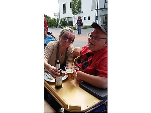Eine Frau hilft einem Mann im Rollstuhl beim trinken.