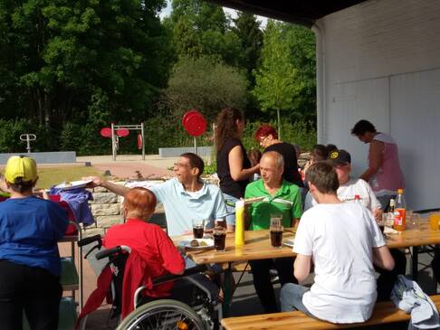 Mehrere Personen sitzen an Tischen in der Sonne.
