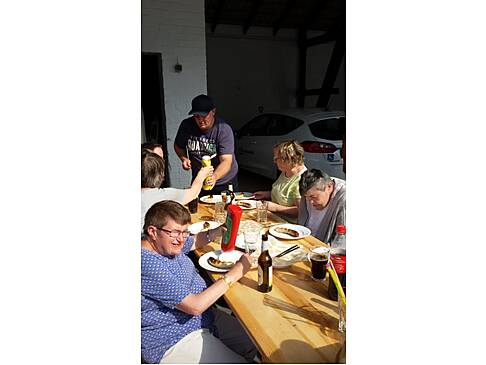Mehrere Personen sitzen an Tischen in der Sonne.