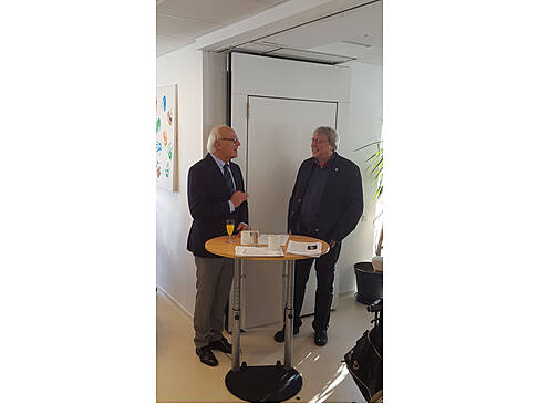 Zwei Männer stehen am Stehtisch und haben ein Mikro in der Hand.