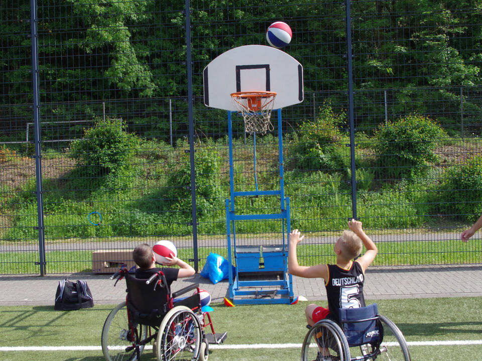 zwei Jungs sitzen im Rolli und spielen Basketball