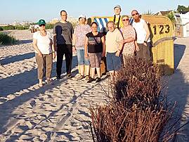 Eine Gruppe von acht Personen steht am Abend im Sand eines Ostseebades neben einem gelben Strandkorb mit der Nummer 123.