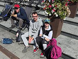 Bild 3: Drei Personen sitzen auf Steinstufen zwischen Liegestühlen und großen Blumenkübeln.