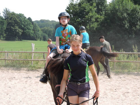 Ein Kind sitzt auf einem Pferd und wird über den Reitplatz geführt.