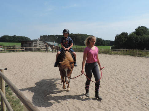 Ein Kind sitzt auf einem Pferd und wird über den Reitplatz geführt.