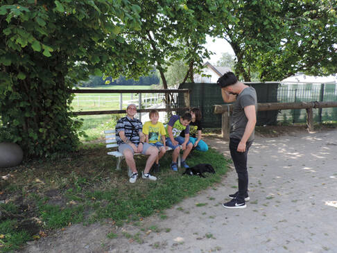 Vier Kinder und Jugendliche sitzen auf einer weissen Bank im Schatten.