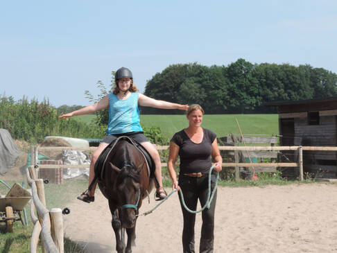 Eine Frau macht eine Übung auf einem Pferd, eine andere Frau führt das Pferd.