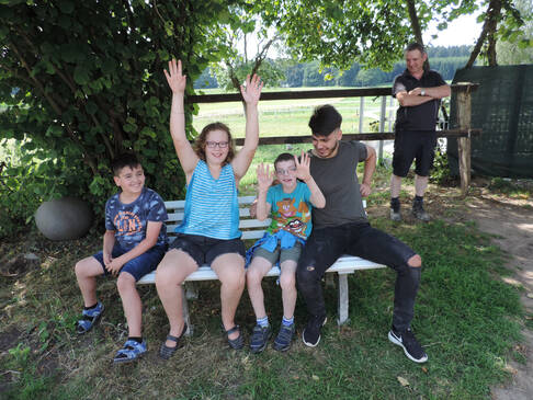 Vier Kinder und Jugendliche sitzen auf einer weissen Bank im Schatten.