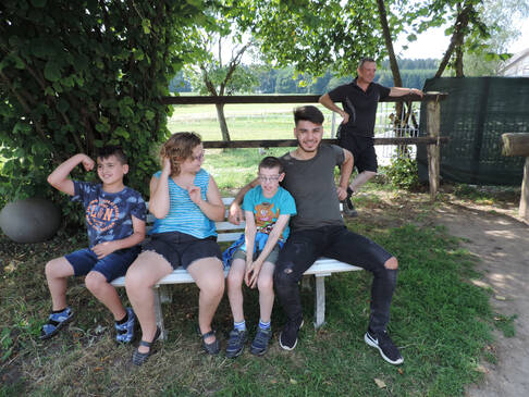 Vier Kinder und Jugendliche sitzen auf einer weissen Bank im Schatten.