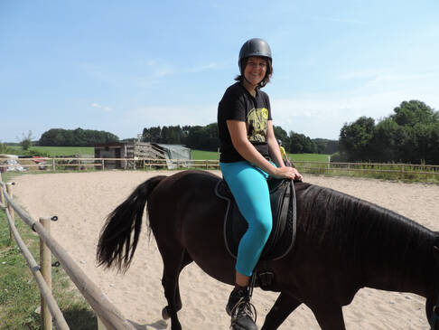 Eine Frau sitzt auf einem Pferd und lacht.