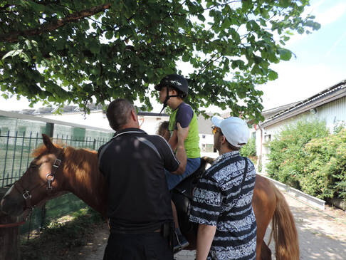 Ein Kind sitzt auf einem Pferd und wird von einem Mann festgehalten, daneben steht eine Frau.