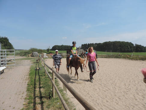 Ein Kind sitzt auf einem Pferd und wird über den Reitplatz geführt.