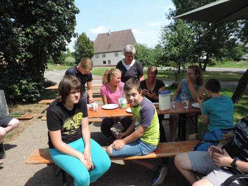Eine Gruppe Menschen sitzt auf einer Holzbank an einem Tisch.