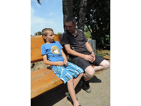 Ein Junge und ein Mann sitzen auf einer Bank in der Sonne.