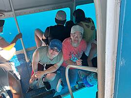 Mehrere Personen sitzen auf einem Ausflugsboot mit Blick auf türkisblaues Wasser. Die Gruppe befindet sich im unteren Bereich des Bootes.