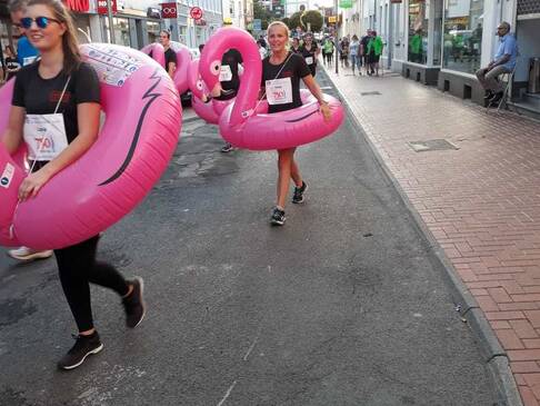 Zwei Persosonen mit Flamingoschwimmreifen laufenüber die Straße.