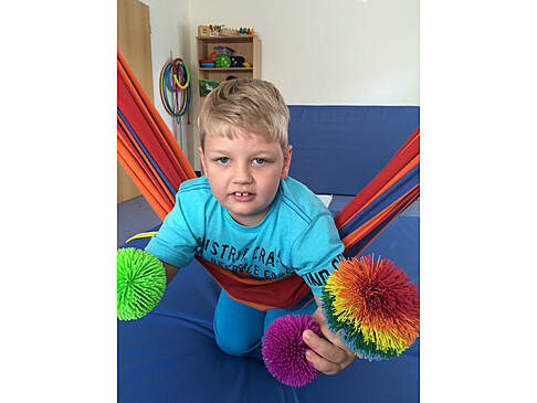 Ein Junge kniet auf Matten und lehnt sich in eine Hängematte.