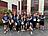 Eine große Gruppe von rund 20 Läuferinnen und Läufern in dunkelblauen „Never Walk Alone"-Shirts posiert lächelnd vor einem Gebäude – viele zeigen Peace-Zeichen oder winken in die Kamera. Es ist das Startfoto des Lebenshilfe-Teams beim Firmenlauf 2026 in Lüdenscheid.