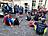 Eine größere Gruppe erschöpfter und erholter Läuferinnen und Läufer versammelt sich nach dem Lauf auf einem Pflasterplatz – einige sitzen auf dem Boden, andere stehen im Gespräch zusammen. Mehrere Personen tragen Shirts der Lebenshilfe Lüdenscheid – Märkischer Kreis mit dem Aufdruck „Gemeinsam stark. Auf jeder Strecke."
