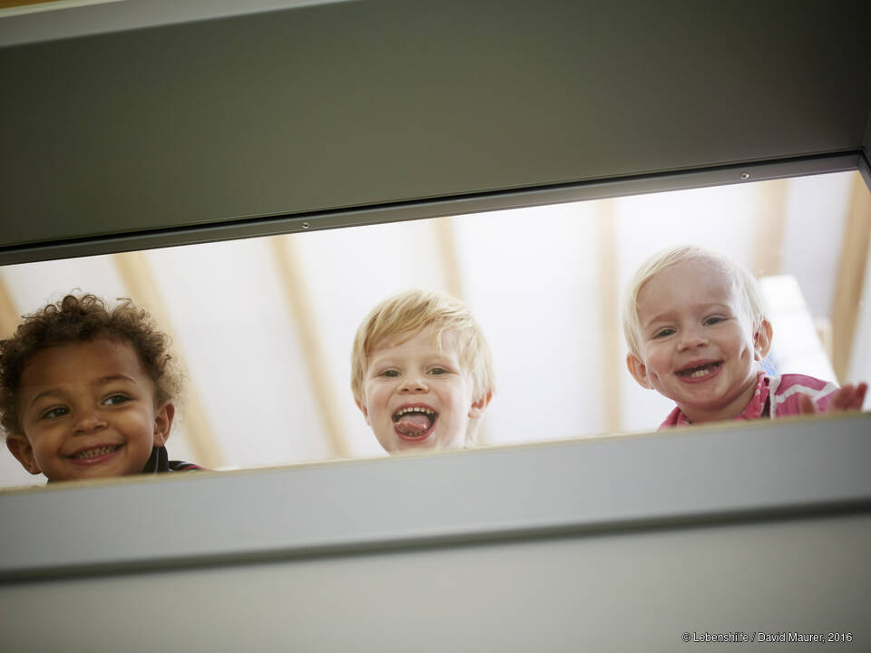 Drei Kinder schauen durch ein Fenster.