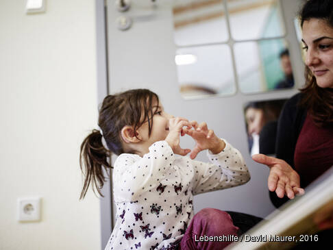 Ein Kind schaut eine Frau an und zeigt mit den Händen etwas.