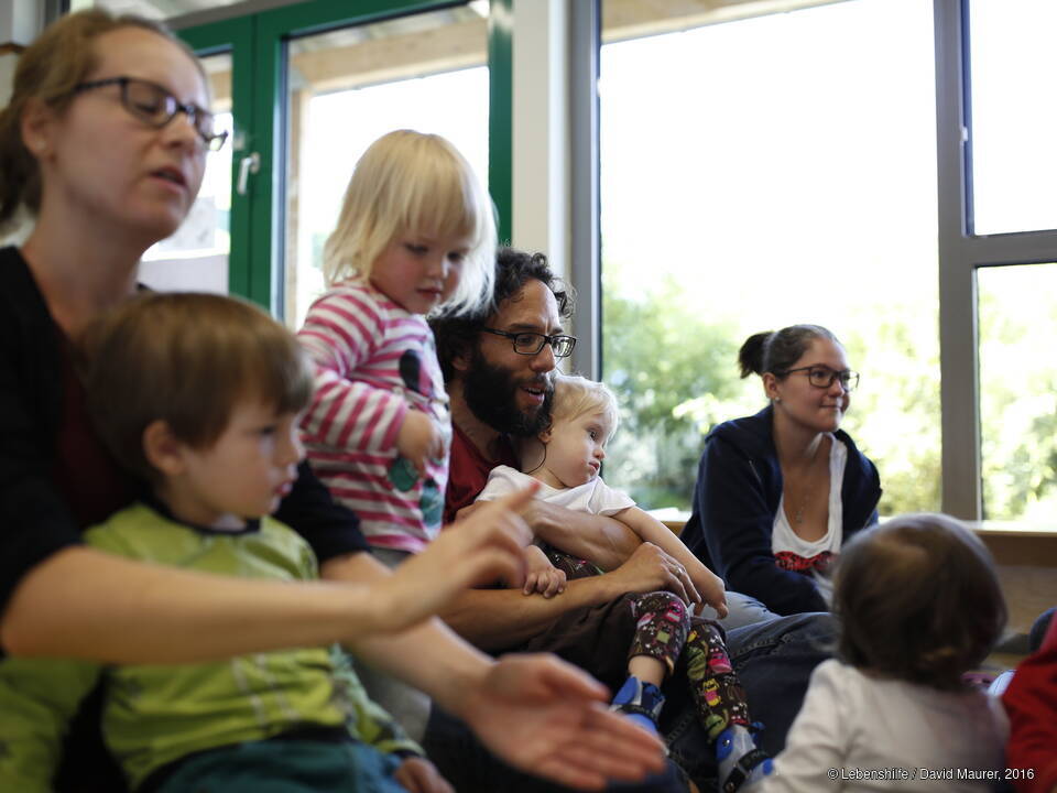 Kinder und Erwachsene sitzen auf dem Boden.