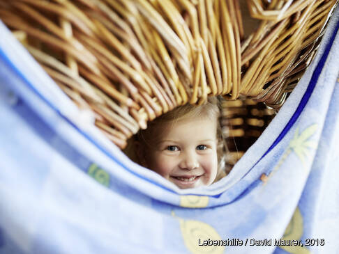 Ein Kind schaut aus einer Bude und lächelt