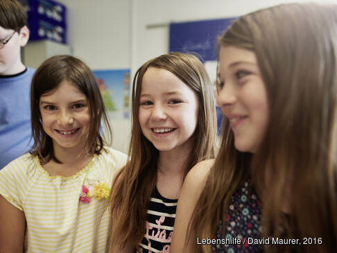 Drei Mädchen und ein ein Junge stehen in einem Raum, die Mädchen lachen.