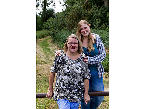 Zwei Frauen am Zaun auf einer Wiese lachen.