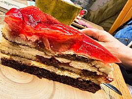 Ein Stück mehrschichtiger Kuchen (mit roten und dunklen Schichten) wird mit einem Kuchenheber angeschnitten.