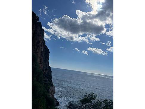Ein hoher Fels und das Meer mit wenigen Wolken und viel Sonne.