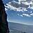 Ein hoher Fels und das Meer mit wenigen Wolken und viel Sonne.