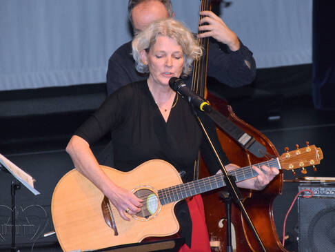 Eine Frau mit einer Gitarre vor einem Mikrofon.