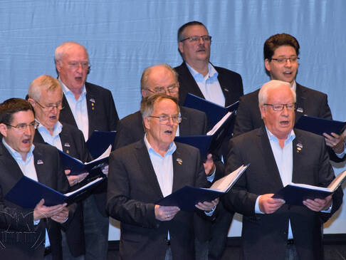 Mehrere Männer mit offenem Buch in der Hand singen.