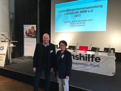 Herr Thiel und eine Frau vor einer Bühne mit einem Tisch.