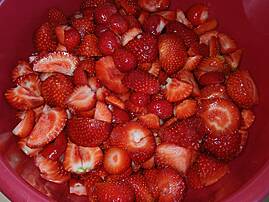 Eine große rote Schüssel gefüllt mit frisch geschnittenen, roten Erdbeeren.
