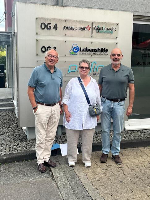 Dr. Wolfgang Schröder, Sibyll Hölscher-Medernach und Christoph Loos (von links nach rechts) stehen als Dreiergruppe vor dem Eingang eines Bürogebäudes. Im Hintergrund ist das Schild der Lebenshilfe Lüdenscheid - Märkischer Kreis zu sehen. Dr. Wolfgang Schröder, Sibyll Hölscher-Medernach und Christoph Loos (von links nach rechts) stehen als Dreiergruppe vor dem Eingang eines Bürogebäudes. Im Hintergrund ist das Schild der Lebenshilfe Lüdenscheid - Märkischer Kreis zu sehen.